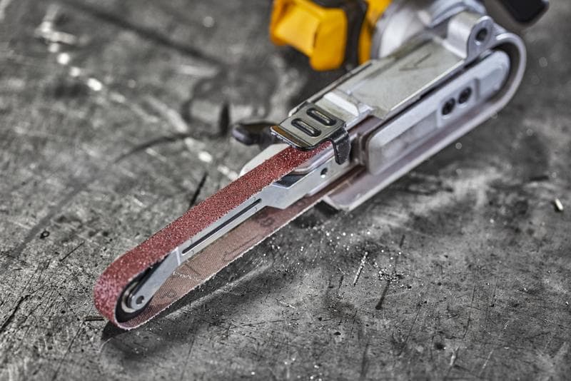 Close-up of a DEWALT electric belt sander on a scratched metal surface.