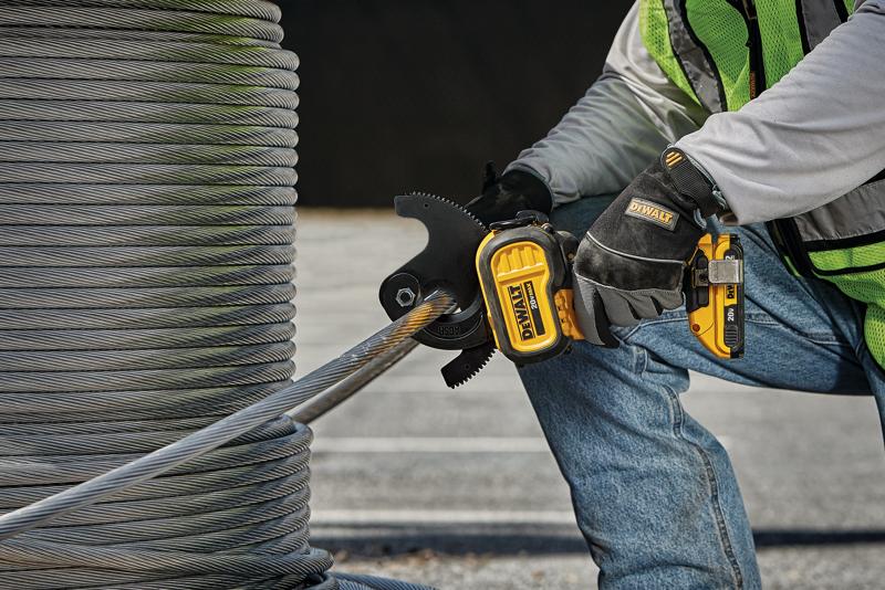 A person wearing work gloves, jeans, and a safety vest uses a DEWALT cordless cable cutter to cut through a thick steel cable coil outdoors.