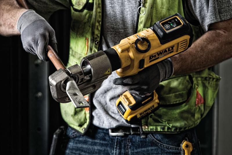 A person wearing gloves and a green safety vest is using a yellow DEWALT battery-powered tool to crimp or cut a metal pipe.