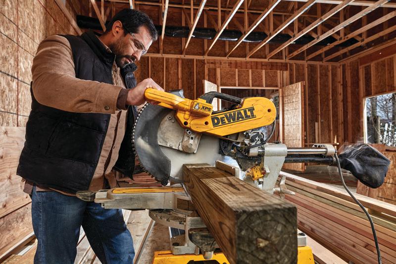 12 inch double bevel sliding compound miter saw being used to cut a thick piece of wood by a worker.