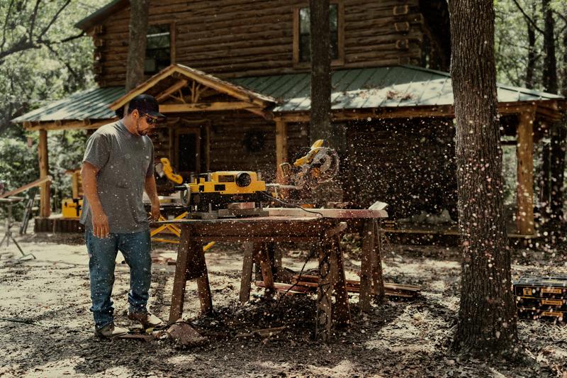 Outdoor woodworking with miter saw and planer, craftsman at log cabin in a forest setting