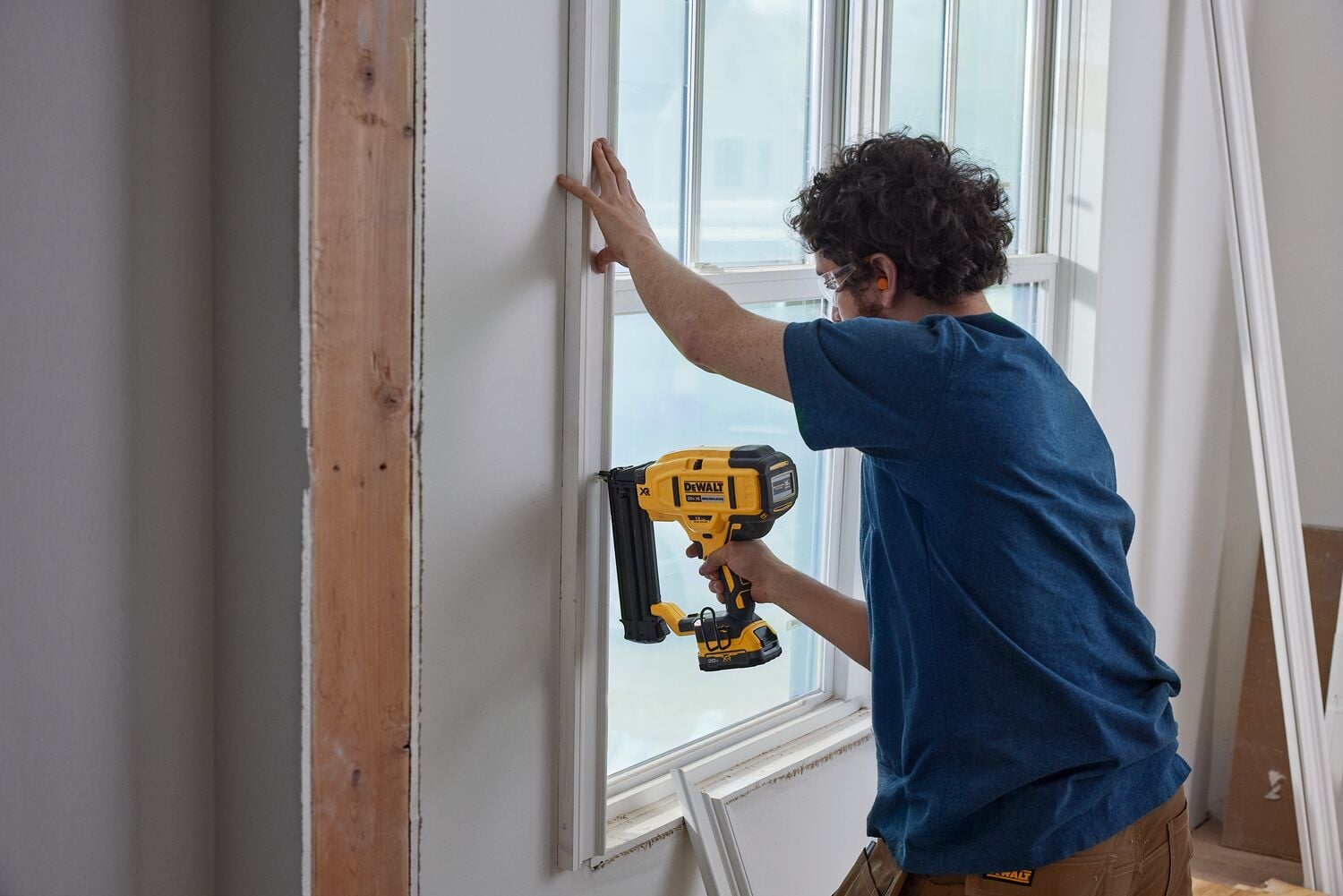 A carpenter uses a nailer on a window frame