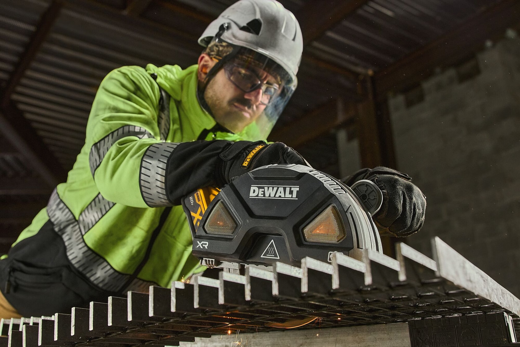 A worker wearing safety gear uses a DEWALT power tool to cut through a metal grate in an industrial setting. The DEWALT branding is visible on the tool.