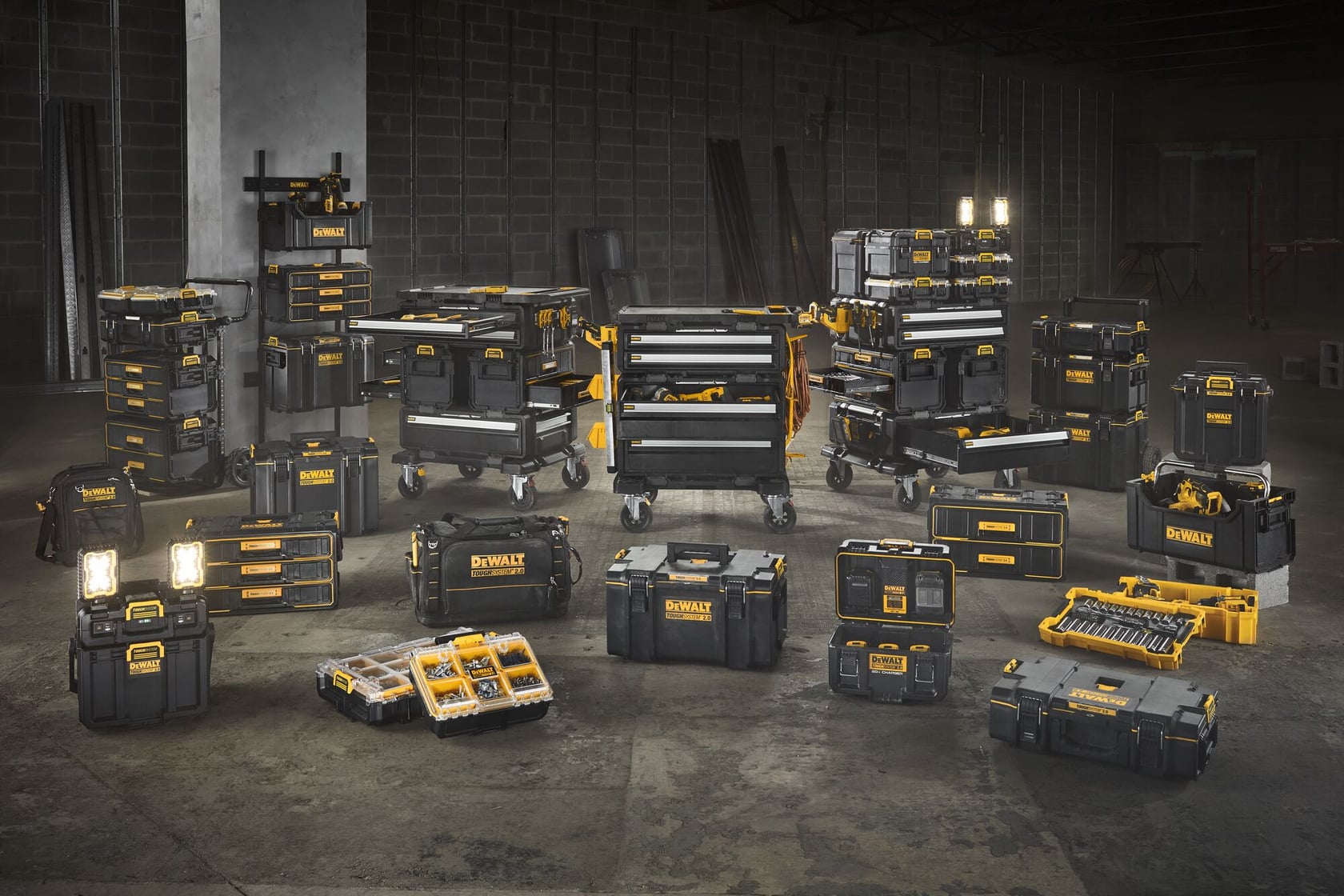 Various DEWALT branded black and yellow tool storage boxes, organizers, and rolling tool cabinets are arranged in a warehouse setting. The products are displayed in groups, showing an assortment of toolboxes, portable cases, organizers, and work lights, highlighting the versatility and storage capacity of the DEWALT tool storage solutions.